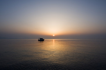 Naklejka na ściany i meble Small fishing boat at sunrise on a calm sea
