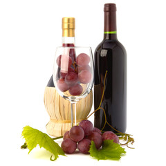wine glass full with grapes and two wine bottles