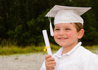 Young boy with cap and gown and certificate for graduation