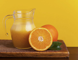 Orange juice in pitcher and oranges. Isolated on yellow