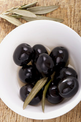 Black olives in  bowl  white on a wooden table