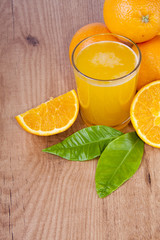 vaso con zumo de naranja, naranjas y hojas verdes