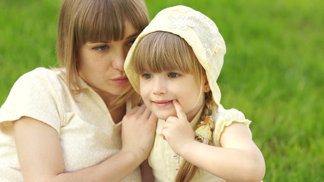 Mother and daughter sitting on the grass and whispering
