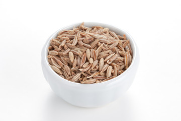 Cumin seeds in a white bowl on white background.