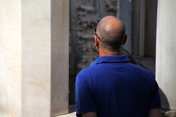 Hombre adulto calvo vestido de azul visto desde detrás