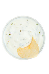 Close up of a bowl of white dip with herbs and a chips dipped in