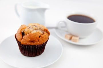 Muffin and a cup of coffee on white plates with sugar and milk