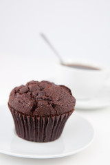 Chocolate muffin and a cup of coffee with a spoon on white plate