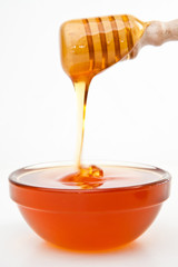Honey on a honey dipper dropping in a bowl