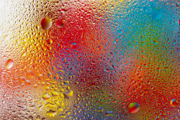 Wassertopfen auf einer Glasscheibe vor farbigem Hintergrund