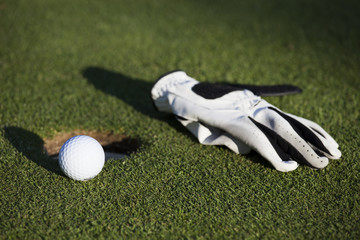 Balle et gant de golf près d'un trou
