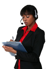 Woman wearing a headset and writing on a clipboard