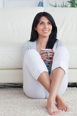 Woman sitting against a couch holding a mug