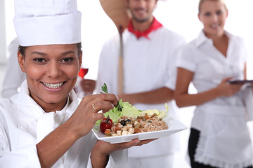 a cook holding a dish, a pizza cook and a waitress