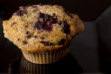 A freshly baked blackberry muffin on a black background