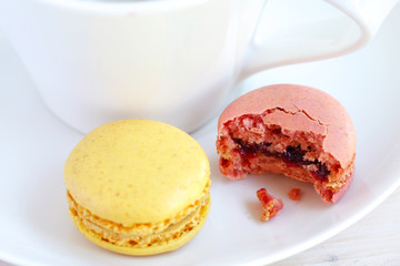 Raspberry and lemon macaroon with white coffee cup, bitten