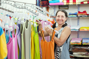 Mature woman  chooses dress at  shop