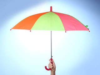 Multi-colored umbrella in hand on blue background