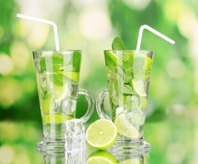Glasses of cocktail with lime and mint on green background