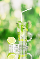 Glass of cocktail with lime and mint on green background