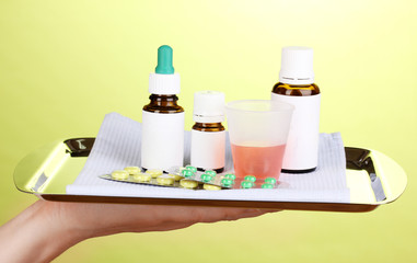 Hand holding tray with medicines on green background