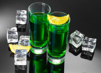 Two glasses of absinthe, lemon and ice on grey background