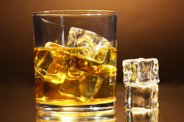 glass of whiskey and ice on brown background
