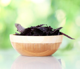 Basil in a wooden bowl on bright green background