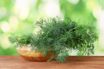 Dill in a wooden bowl on green background