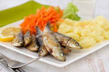 fried sardines with salad and mashed potato on the plate
