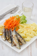 fried sardines with salad and mashed potato on the plate