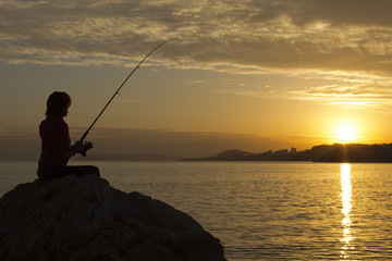 Happy girl fishes at sunset, near the sea at sunset