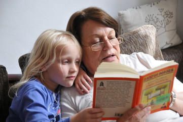Großmutter ließt Enkeltocher etwas aus einem Buch vor