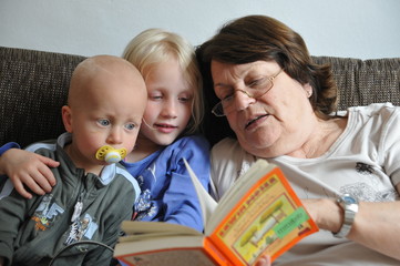 Großmutter ließt zwei Enkelkindern aus einem Buch vor