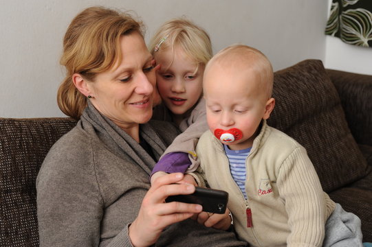 Mutter mit zwei Kindern zeigt etwas auf dem Smartfon