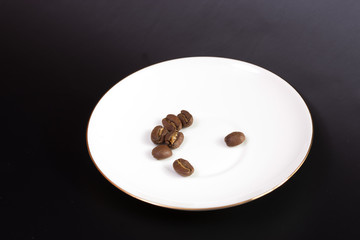 a few coffee beans on a white plate on a black background