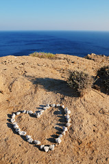 Heart of stones on the sand in front of the blue sea