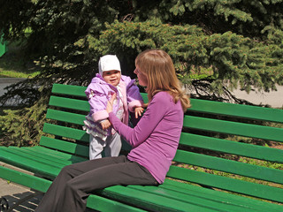 Мама с дочкой сидят на скамейке в парке