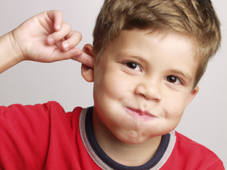 Retrato de un niño feliz y expresivo tocándose el oído. - obrazy, fototapety, plakaty
