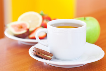 cup of tea,cookie,apple, lemon, fig and strawberries on a plate