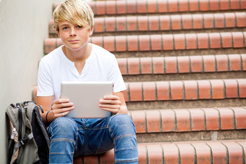 teen boy sitting on stairs and using tablet computer in school