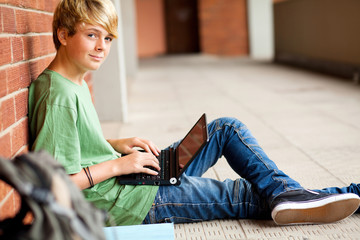 teen student using laptop in school passage