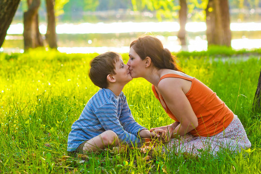 Mom and son of woman and child sitting on grass kissing at sunse
