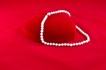 Cofanetto cuore rosso e collana di perle su fondo rosso