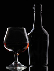 Glass of brandy and bottle on black background