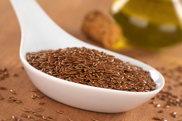 Brown flax seeds on ceramic spoon with linseed oil