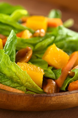Spinach, mango, carrot salad with peanuts on wooden plate