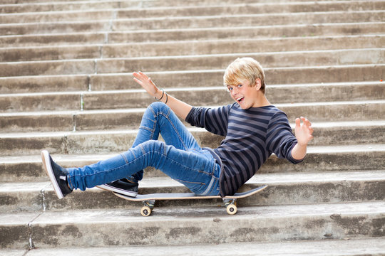 playful teen boy sitting on skateboard