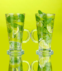 Glasses of cocktail with lime and mint on green background