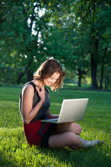 Woman sits on grass with laptop